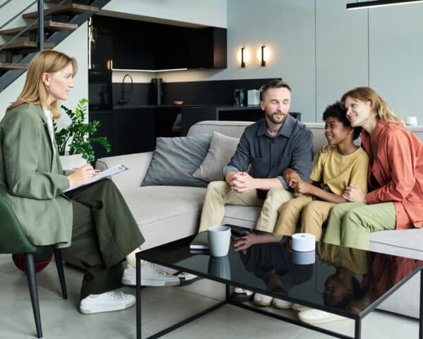 Image of a family consisting of caregivers (Parents) and adopted/foster child interacting with a counselor in their home.